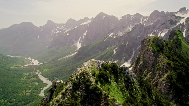 Aerial view of magnificent mountains in Albania - edge of cliff at Valbona Pass, Albanian Alps. Morning in the mountains, rocky peaks with snowfields, popular place for trekking and hiking