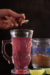 Hand stirring the sugar in a tea cup on a black table with a green sliced lemon and a sugar pot