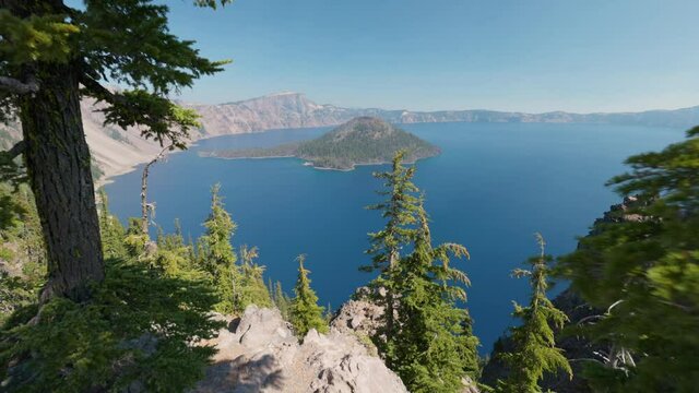 Crater Lake National Park, Oregon, USA. Camera moves between the tree trunks, view of the blue lake and the island. Gimbal shot, 4K