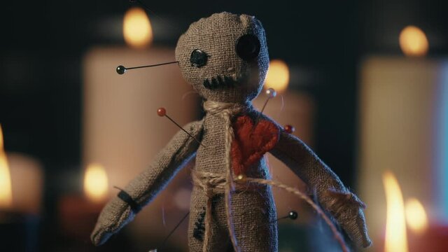 Voodoo Magic concept. Voodoo doll studded with needles with pierced rag heart and around burning candles. Spooky or eerie magical esoteric ritual.