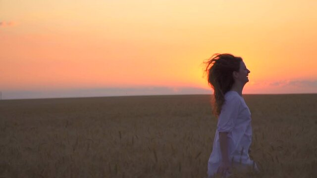 Beautiful caucasian woman run to side field. girl is dancing in nature. Mother nature. Have fun at sunset. sun is golden on horizon. Touch wheat with your hand. Romantic dress camera to side to right 