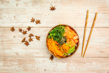 Top view image of poke bowl of Norwegian salmon with masago roe, carrot zest, ripe avocado, pumpkin seeds and wakame salad to eat with wooden chopsticks