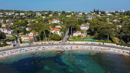 Fototapeta na wymiar Aerial view of expensive estates behind Ondes Beach on the Cap d'Antibes in the French Riviera - Tourists sunbathing by the Mediterranean Sea in the South of France