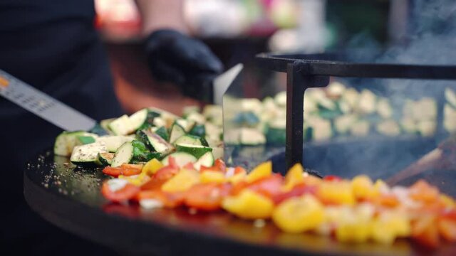 Close up shot of cut zucchini, onion, red and yellow bell peppers grilling on professional bbq smoker grid seasoned with aroma spices and herbs, process of preparation vegetables on bbq grill outdoor