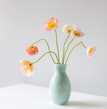 Close up of pink poppies in green vase on white table against grey background