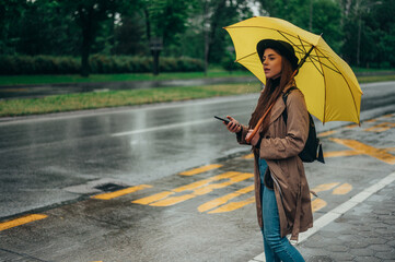 Woman holding yellow umbrella and using smartphone while on a bus stop
