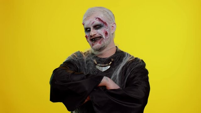 Cheerful happy creepy man with bloody scars face, Halloween stylish zombie make-up. Scary wounded undead guy making faces, looks at camera and smiles terribly with dirty teeth. Sinister beast, monster