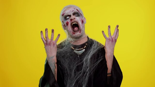 Sinister man in carnival costume of Halloween crazy zombie with bloody wounded scars face screaming, shouting, trying to scare on chroma key. Horror theme of cosplay wounded undead, beast, monster