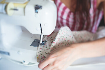 Process of hemming the dress and pants at home, close up of cloth on the sewing machine, hemming, tailoring, repairing and stitching cloth and dress, with the hand of female dressmaker in background