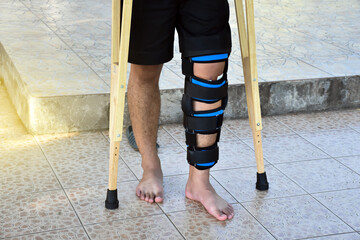 A man who has a left broken leg which wrapped with knee pad walks on crutches on the floor. Broken...