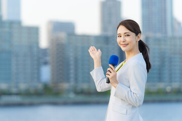 都市の前に立つ女性アナウンサー