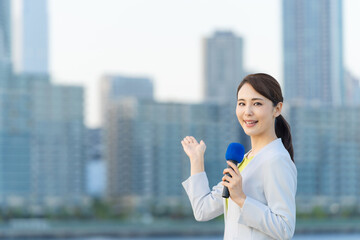 都市の前に立つ女性アナウンサー