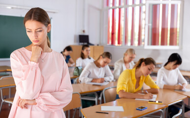 Upset girl standing during classes in auditorium with fellow students on background