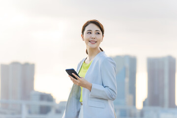 都市を背景にスマホを持つ女性