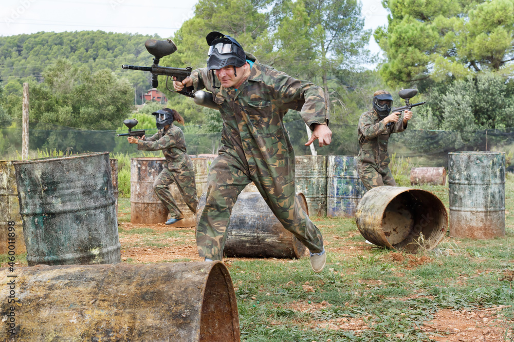 Poster Paintball players aiming and shooting with a guns at the opposing team outdoors