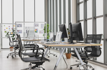 Meeting room with multiple glass windows and conference tables with laptops and desktops on in office