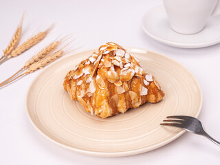 side angle of fresh croissant covered almond slide mixed sweet caramel and topping with sugar powder on a pastel plate placed on white table top.