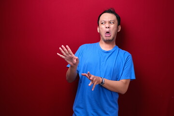 Young asian man is surprised and mad with looking right isolated on red background.