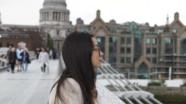 Young woman looking over the River Thames from Millennium Bridge with St Pauls Cathedral in the background