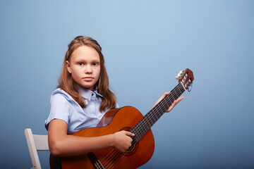 Fototapeta premium an 11-year-old girl is practicing a melody on a guitar on a blue background