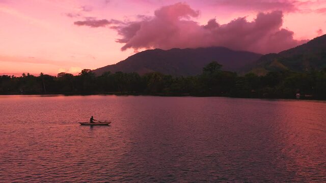 A father paddeling his canoe returning home in the evening after fishing out in the sea.