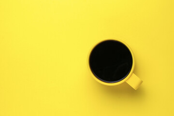 Yellow mug with black coffee on a yellow background. Flat lay.