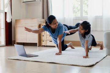 Asian young mother and her daughter doing stretching fitness exercise yoga together at home. Parent...