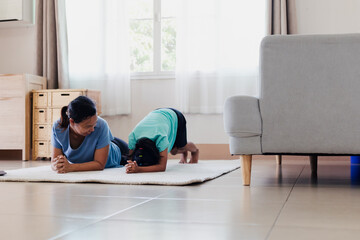 Asian young mother and her daughter doing stretching fitness exercise yoga together at home. Parent teaching child work out to be strong and maintain physical health and wellbeing in daily routine.