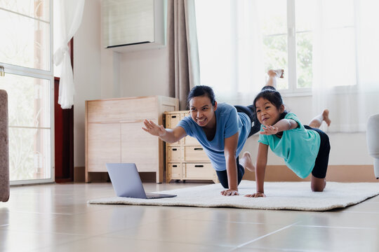 Asian young mother and her daughter doing stretching fitness exercise yoga together at home. Parent teaching child work out to be strong and maintain physical health and wellbeing in daily routine.