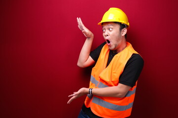 Young asian man worker is surprised and shouting wow with pointing right with his hand isolated on red background. - obrazy, fototapety, plakaty