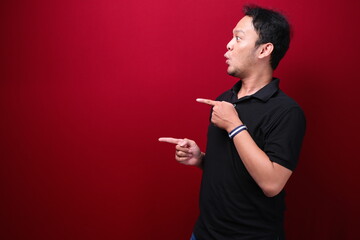 Young asian man is surprised and shouting wow with pointing right with his hand isolated on red background.