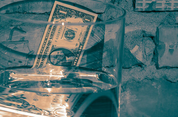 Paper dollar against background of brickwork with mortar through prism of glass vessel filled with water with partially distorted image of bill. Drowning American dollar.  Selective focus.