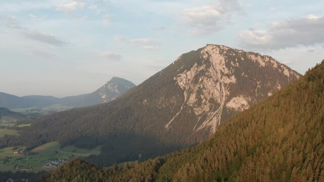 Aerial view of mountainside forest and a sunlit peak, in Unternberg alps, sunset in Austria - rising, drone shot