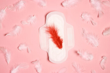 Menstrual pad with red and white feathers on pink background.