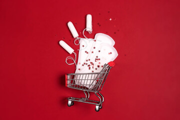 Shopping cart with menstruation period accessories on red background. Sanitary pads, tampons and...