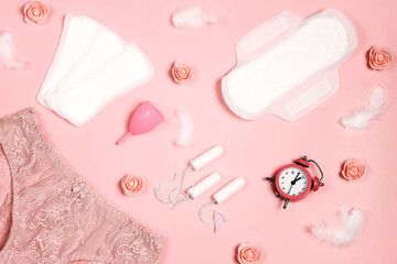 Women's panties with sanitary napkins, tampons, menstrual cup, flowers and feathers on pink background. Different types of feminine hygiene products