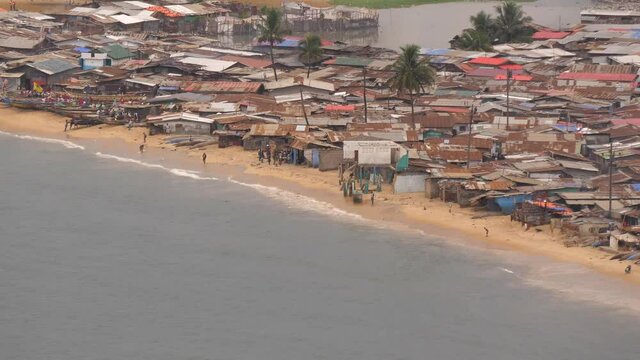 People, boats, and shacks on West Point beach in Liberia, Monrovia next to Atlantic Ocean - telephoto from far