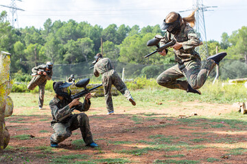 Dynamic paintball battle. Portrait woman player jumping and aiming marker on player of opposing team