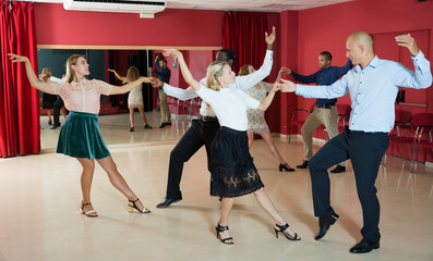 Adult dancing couples enjoying active boogie-woogie in modern studio..