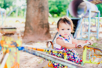 A picture of an Asian child playing on the outdoor carousel alone.