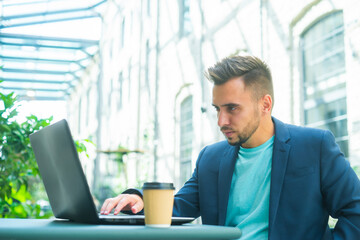 Young successful caucasian businessman works in an outdoor cafe using a computer. Business, freelance and remote work.