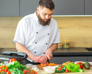 Young chef is cutting fish in a modern kitchen. The man prepares food at home. Cooking healthy and...