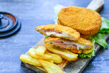 
 Crispy  deep fried home made     chicken Cordon bleu with cheese   and ham  and french fries on wooden rustic background.  