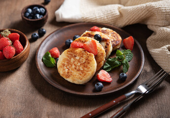 Cottage cheese pancakes with mint, blueberries and strawberries on a dark wood background. Healthy and delicious breakfast