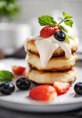 Homemade Russian dish for breakfast  syrniki or cottage cheese pancakes in a stack with fresh mint and berries close-up on a blurry light gray background. The concept of healthy breakfast. Macro view