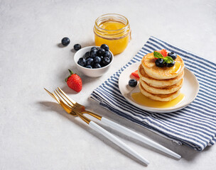 Homemade classic American pancakes in a stack with fresh berries and honey on a striped napkin on a light gray texture background. The concept of a healthy and dietary breakfast. Space for text