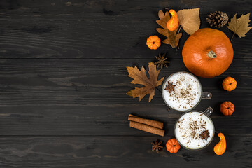 Spice pumpkin latte with cream foam, cinnamon stick, leaf and orange pumpkins on wooden background, copy space.