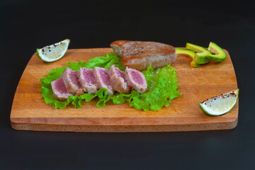 fried tuna steak cut into pieces lies on a wooden board on a black background. The concept of a healthy diet, a source of protein, useful trace elements, vitamins and omega.