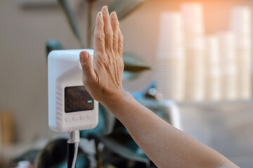 Customer raised hand at digital thermometer with temperature scanning machine for fever before entering area. Screening to prevent infected people from entering restricted areas. Covid-19 concept.