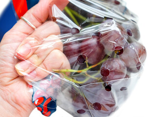 The hand stretches the package of grapes. Show package